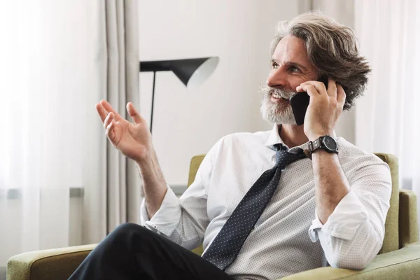 Image of joyful mature man talking on cellphone while sitting on — Stock Photo, Image