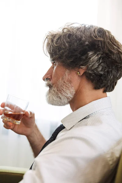 Handsome senior gray-haired business man sitting in chair indoors at home drinking alcohol. — Stock Photo, Image