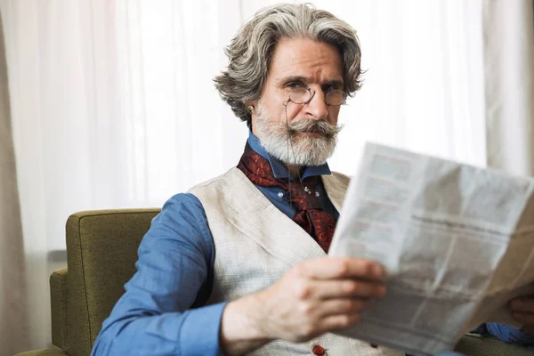 Porträt eines attraktiven erwachsenen Geschäftsmannes, der Zeitung liest, während er im Sessel seines Hotelappartements sitzt — Stockfoto