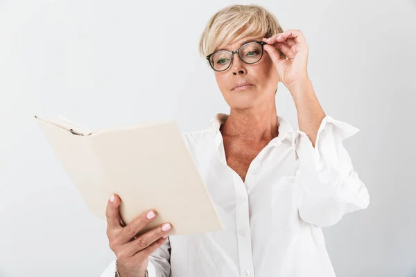 Portrait of serious adult woman wearing eyeglasses reading book — Stock Photo, Image