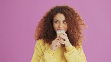 Pensive genç kızıl saçlı kadın gülümseyen ve pembe arka plan izole üzerinde kahve içme