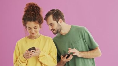 Yakışıklı genç sakallı brunet adam kız arkadaşının akıllı telefon bakarak ve hoşnutsuz olma. Sevimli genç kızıl saçlı kıvırcık kadın erkek arkadaşı ndan akıllı telefon gizleme. Pembe arka plan üzerinde akıllı telefonlarını kullanan güzel gülümseyen genç çift
