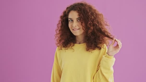Zamyšlená Mladá Kudrnatá Žena Usmívá Pohrává Vlasy Růžovém Pozadí Izolované — Stock video