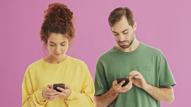 Привлекательная Улыбающаяся Молодая Пара Разговаривает Смеется Используя Свои Смартфоны Розовом — стоковое видео