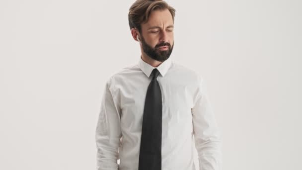 ワイヤレスイヤホンを持つハンサムな若いひげのビジネスマンは 灰色の背景の上にスマートフォンに呼び出しを持っています — ストック動画
