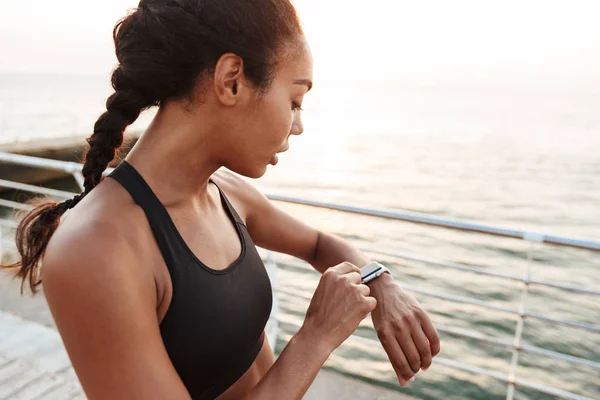 Bild einer athletischen hübschen Frau, die auf ihre Armbanduhr blickt, während sie — Stockfoto