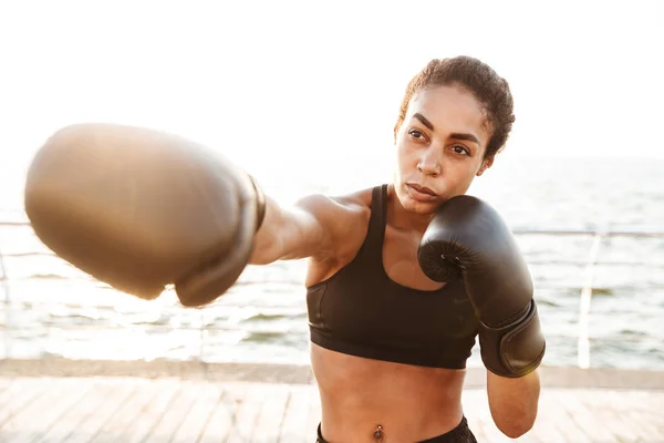 Image d'une jolie femme sportive s'entraînant en gants de boxe par mer — Photo