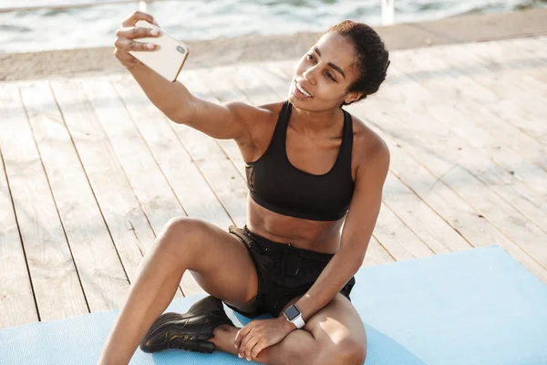 Foto de una mujer afroamericana tomando selfie en un smartphone mientras —  Fotos de Stock