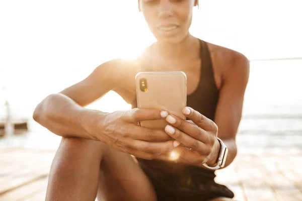 바다가 앉아있는 동안 스마트 폰을 들고 햇빛이 비치는 여성의 사진 — 스톡 사진