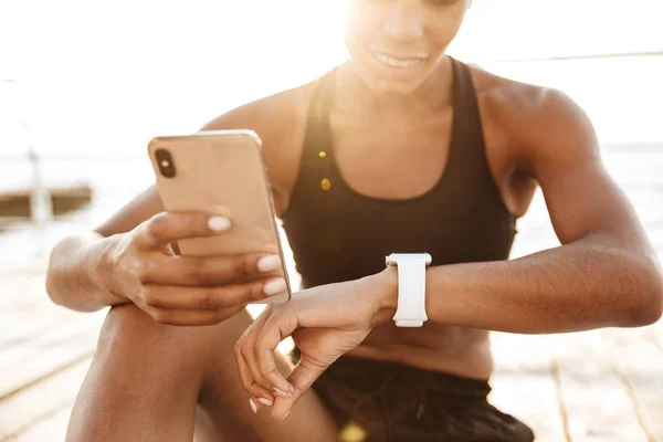 Foto de mulher atraente segurando smartphone e olhando para pulsos — Fotografia de Stock