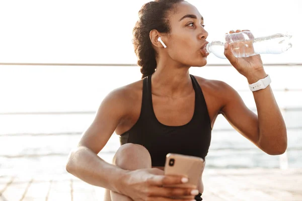 Foto di attraente donna che tiene smartphone e acqua potabile — Foto Stock