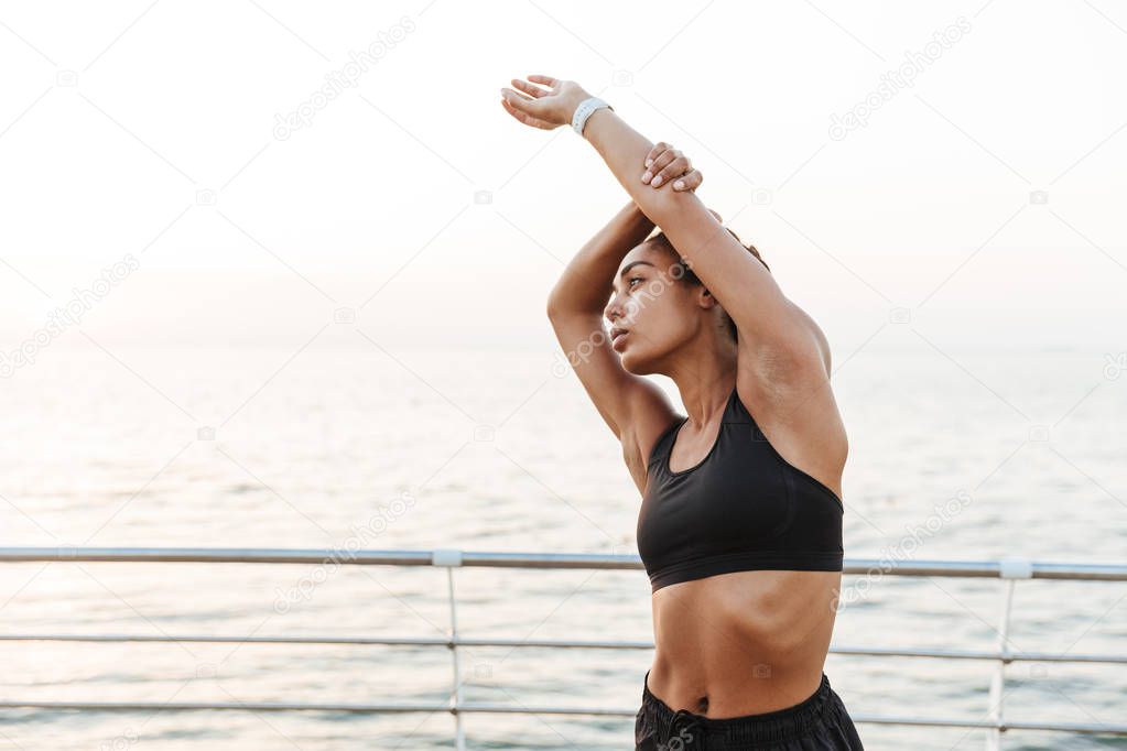 Image of african american fitness woman stretching her arms whil