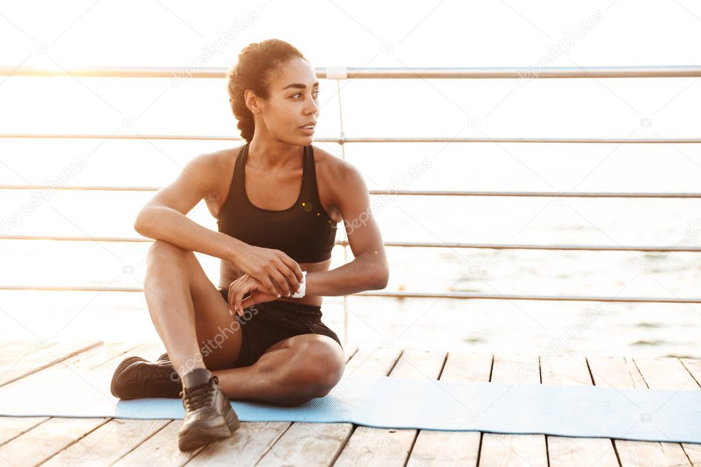 Image of slim woman sitting on finess mat and touching wristwatc