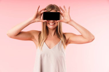 Mutlu genç kadın görüntü elbise gülerek ve yüzüne akıllı telefon tutarak