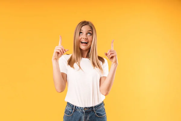 Imagen de una mujer rubia alegre usando una camiseta casual sonriendo a la cámara y señalando con los dedos al espacio de copia — Foto de Stock