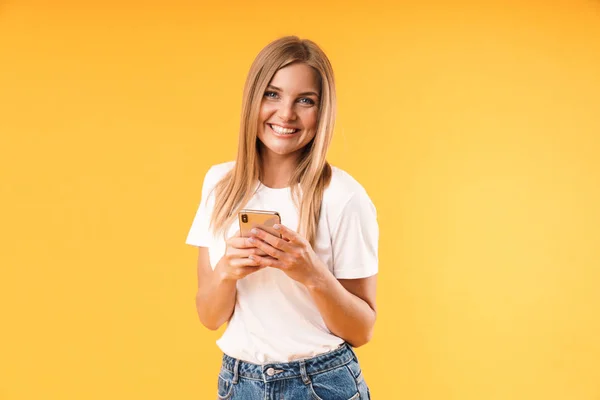 Immagine primo piano della giovane donna bionda che indossa una t-shirt casual sorridente mentre usa lo smartphone — Foto Stock