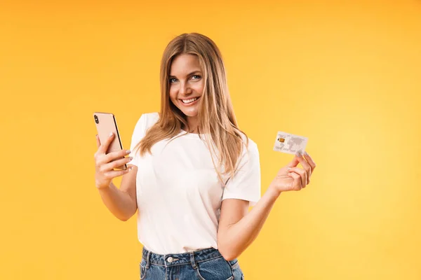 スマートフォンやクレジットカードを持ちながら笑顔のカジュアルなTシャツを着た楽観的なブロンド女性の画像クローズアップ — ストック写真