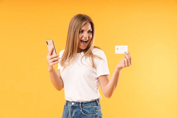 Bild Nahaufnahme einer fröhlichen blonden Frau in lässigem T-Shirt, die schreit, während sie Smartphone und Kreditkarte in der Hand hält — Stockfoto