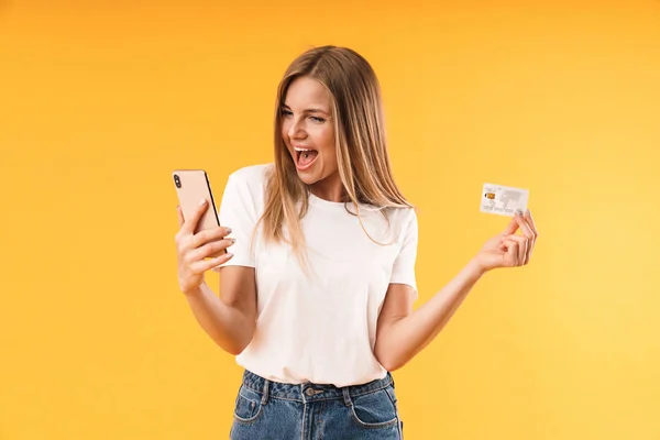 スマートフォンやクレジットカードを持ちながら悲鳴を上げるカジュアルなTシャツを着た喜びのブロンド女性の画像クローズアップ — ストック写真