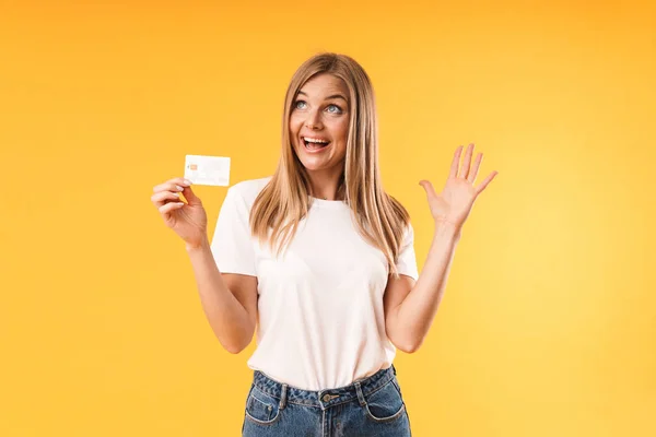 Immagine primo piano di una donna bionda positiva che indossa una t-shirt casual sorridente mentre tiene in mano la carta di credito — Foto Stock