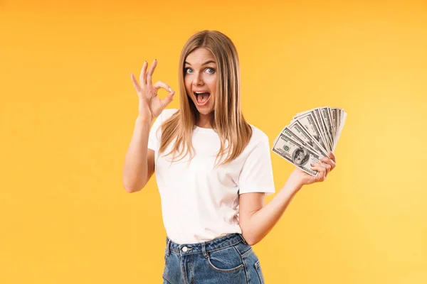 Image gros plan d'une femme blonde heureuse portant un t-shirt décontracté montrant un signe ok tout en tenant de l'argent comptant — Photo