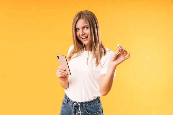 Зображення крупним планом позитивної блондинки, яка посміхається під час прослуховування музики зі смартфонами та навушниками — стокове фото