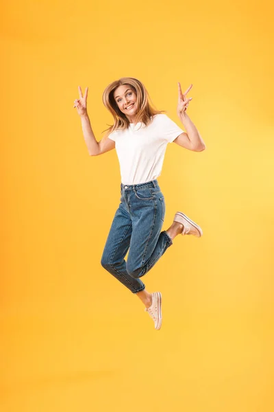 Imagen completa de la mujer rubia feliz usando una camiseta casual sonriendo a la cámara y mostrando los dedos de la victoria —  Fotos de Stock