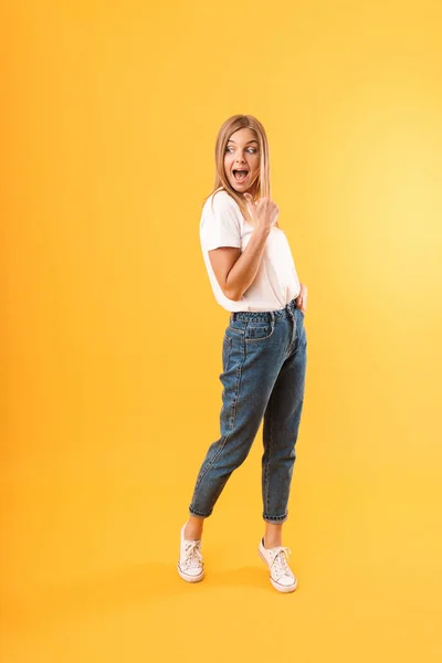 Full length image of beautiful blond woman smiling at camera and pointing finger at copyspace — Stock Photo, Image