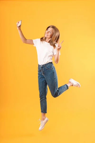 Volledige lengte afbeelding van Happy blond vrouw tonen vrede vingers terwijl het nemen van selfie foto — Stockfoto