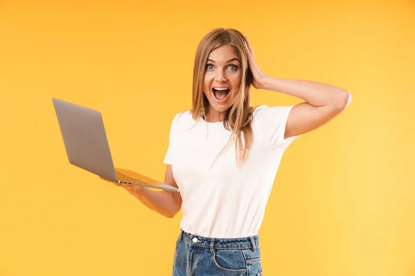 Εικόνα της ξαφνιωμένη ξανθιά γυναίκα φορώντας περιστασιακή t-shirt εκφράζοντας το θαύμα κατά τη χρήση του φορητού υπολογιστή — Φωτογραφία Αρχείου
