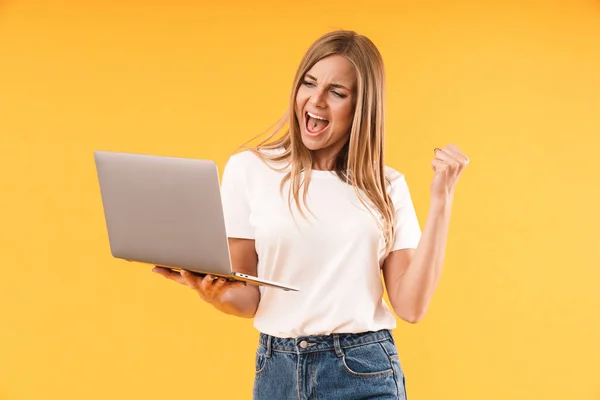 Imagen de una hermosa mujer rubia que usa una camiseta casual expresando victoria mientras usa una computadora portátil — Foto de Stock