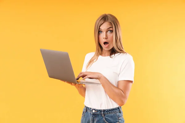 困惑的金发女郎穿着休闲T恤，使用笔记本电脑表达奇迹的图像 — 图库照片