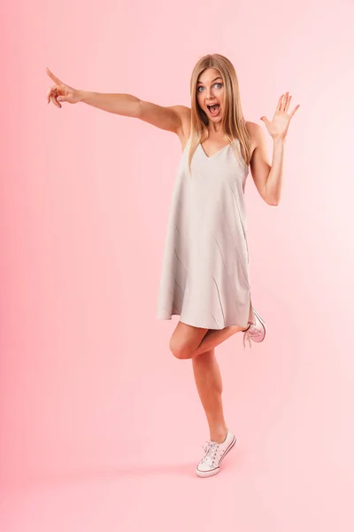 Full length image of happy blond woman expressing wonder and pointing finger at copyspace — Stock Photo, Image
