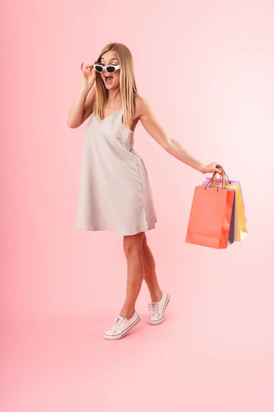 Imagen de longitud completa de mujer joven caucásica con vestido sonriente y llevando coloridas bolsas de compras de papel —  Fotos de Stock