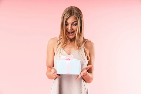 Bild einer fröhlichen jungen Frau, die ein Kleid trägt, das ihrer Überraschung Ausdruck verleiht und eine Geschenkbox in der Hand hält — Stockfoto