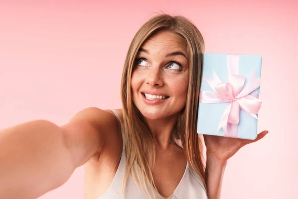 Εικόνα της όμορφης νεαρής γυναίκας που φοράει φόρεμα χαμογελώντας και κρατώντας κουτί δώρου, ενώ λαμβάνοντας selfie φωτογραφία — Φωτογραφία Αρχείου