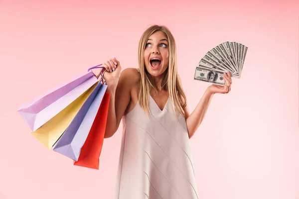 Image of young blond woman smiling while holding colorful paper shopping bags and money bills — Stockfoto