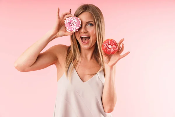 Immagine di una donna bionda gioiosa che indossa un vestito sorridente mentre tiene due ciambelle dolci — Foto Stock