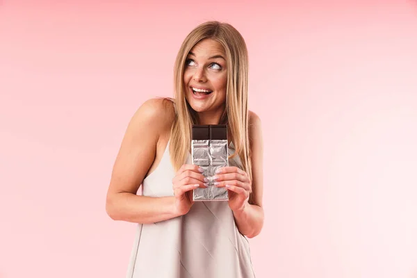 Immagine di una donna bionda positiva che indossa un vestito guardando verso l'alto mentre tiene la barra di cioccolato — Foto Stock
