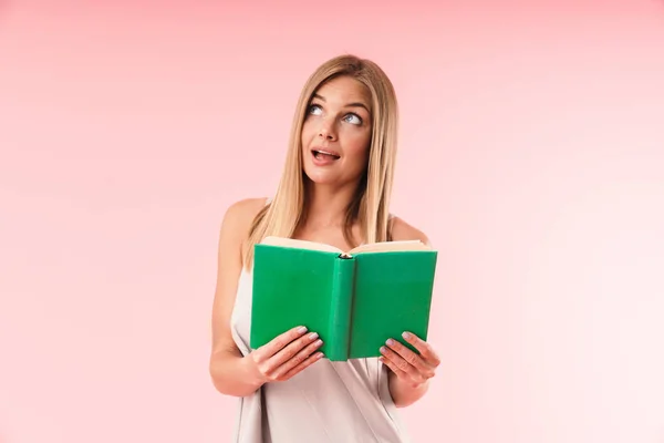 Imagen de mujer rubia alegre usando vestido sonriente y mirando hacia arriba mientras lee el libro —  Fotos de Stock