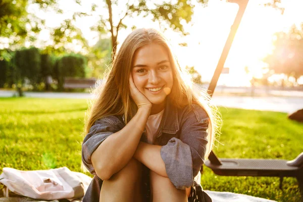 Neşeli gülümseyen genç kız doğa yeşil parkta çim üzerinde oturup. — Stok fotoğraf