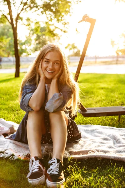 Adolescente chica sentarse fuera en la naturaleza verde parque en la hierba con scooter . — Foto de Stock