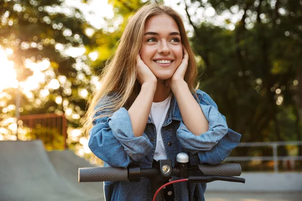 Positivo ottimista giovane ragazza adolescente al di fuori nella natura parco verde a piedi con scooter . — Foto Stock