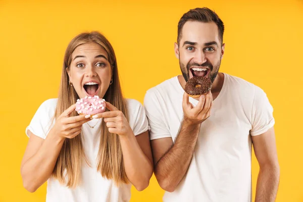 Imagen de pareja complacida sonriendo mientras comen rosquillas dulces juntos — Foto de Stock