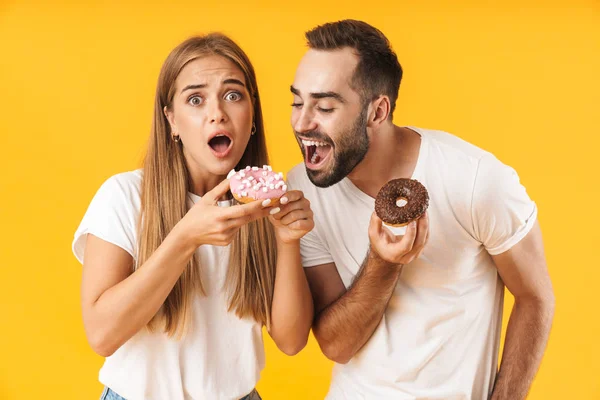 Image of happy couple smiling while eating sweet donuts together — Stock Fotó