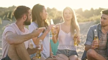 Bir grup neşeli genç arkadaş sahilde konuşurken bira içip pizza yiyorlar.