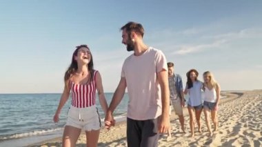 Deniz kenarında yürürken konuşan ve gülen bir grup genç arkadaş.