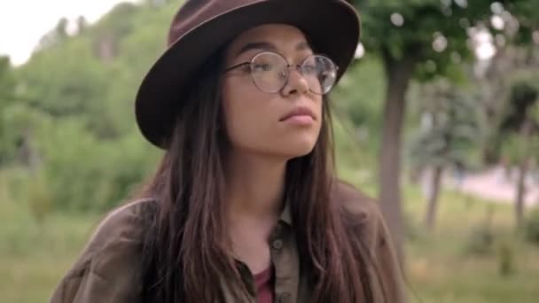 魅力的な穏やかな若いですブルネット女性で茶色い帽子何かについて考えて公園に滞在しながら周りを見回す — ストック動画