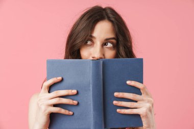 Güzel düşünme genç sevimli kadın kitap ile yüz kapsayan pembe duvar arka plan üzerinde izole poz.