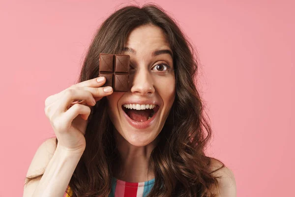 Šťastná mladá roztomilá žena, která pózná na pozadí růžové zdi s čokoládovými sladkoty. — Stock fotografie